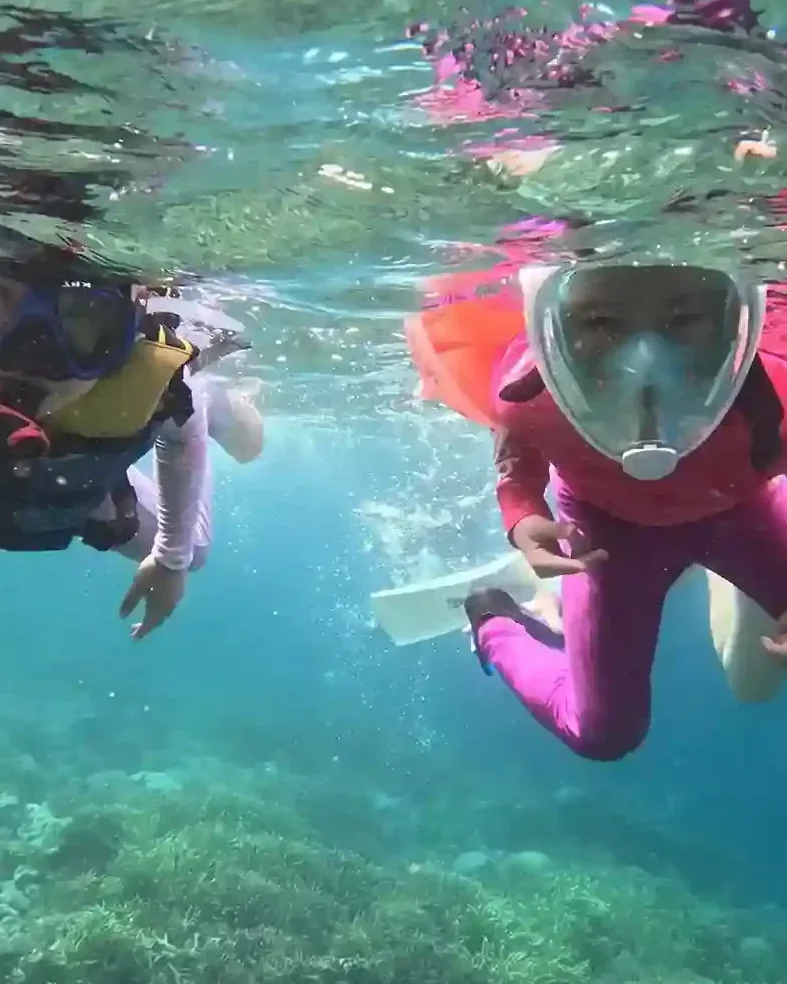 Two children snorkelling in full-face masks over shallow reef